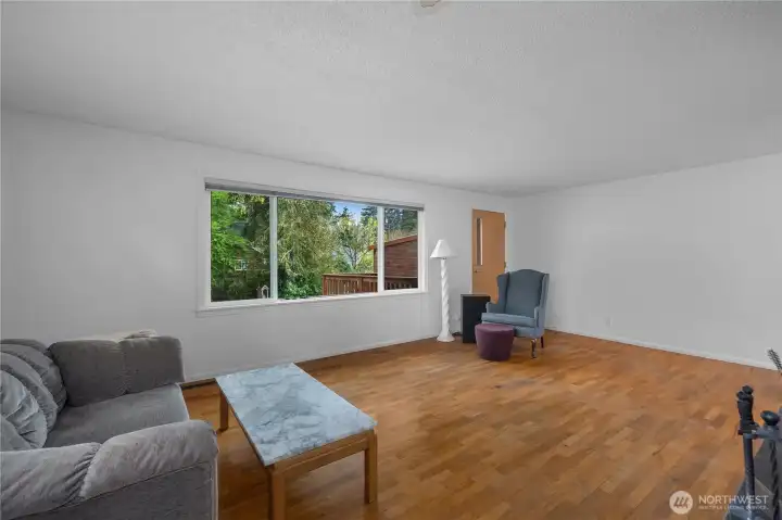 Generous living area featuring hardwood floors and an oversized window overlooking the backyard.
