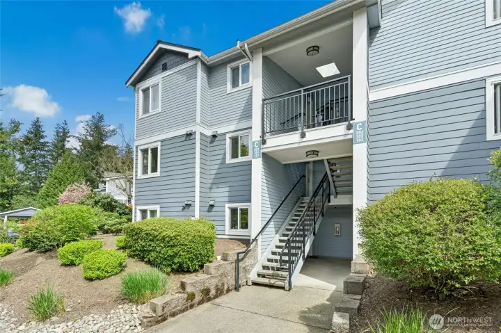 Front exterior with entry access, mature landscaping, and walkway leading to unit.