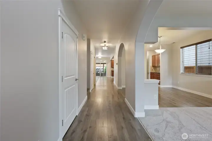 A spacious central hallway with wide laminate wood-style plank flooring and elegant arched openings welcomes you to the main living areas. On the right, discover a bright dining room and a stylish chandelier, plus a versatile flex room currently staged as a music room with a Yamaha grand piano. Neutral tones, and natural light create a seamless, sophisticated flow ideal for both everyday living and entertaining.  This home embodies timeless beauty and luxury.