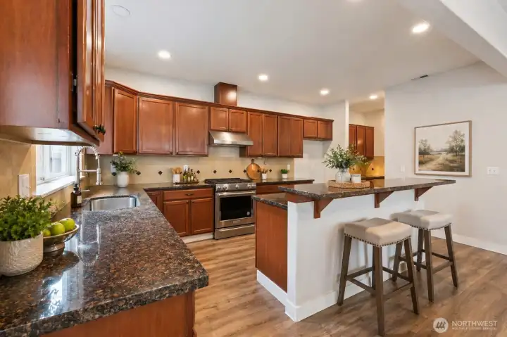 A stunning open-concept kitchen anchored by a generous island with bar seating, showcasing rich cabinetry, gleaming granite countertops, and stainless steel appliances. Designed for connection and entertaining, this space flows effortlessly into the home’s main living areas.