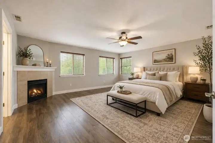 Spacious and serene primary bedroom featuring gleaming hardwood floors, a cozy fireplace with elegant mantel, and abundant natural light. Highlights include a grand upholstered bed, comfortable seating area, ceiling fan, French doors, and sophisticated neutral finishes — creating a luxurious and peaceful retreat.