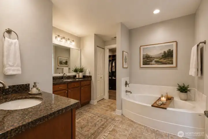 The spa-inspired primary bathroom is a masterpiece of elegance and indulgence. Rich, dark wood cabinetry and gleaming dark granite countertops create a warm, sophisticated foundation. Dual vanities offer generous space for two, each with undermount sinks, brushed nickel fixtures, and abundant storage. Oversized framed mirrors and dramatic vanity lighting bathe the room in beautiful illumination, while the deep soaking tub.  Adjacent is an enormous walk-in closet with premium custom wood shelving offering boutique-level organization and storage. Sophisticated, serene, and exceptionally appointed.