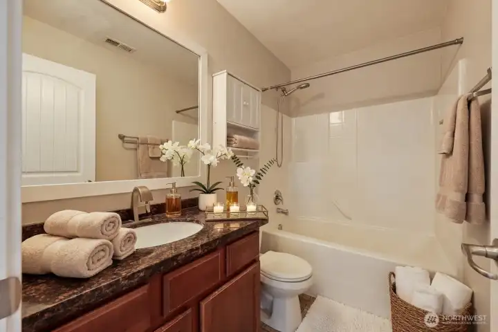 Second bathroom upstairs features a handsome dark granite countertop on cherry wood cabinetry, white undermount sink, and brushed nickel fixtures. Includes a large, framed mirror, wall storage cabinet, and full bathtub with shower.