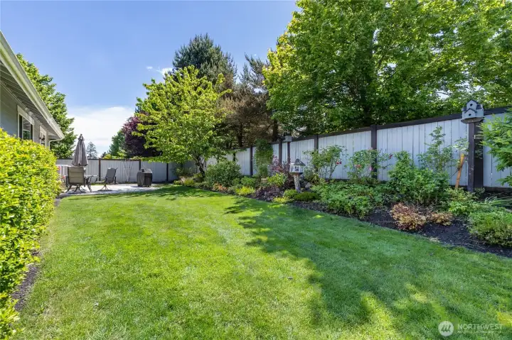 Wide view of the level, fully-fenced backyard surrounded by mature trees and gorgeous landscaping.