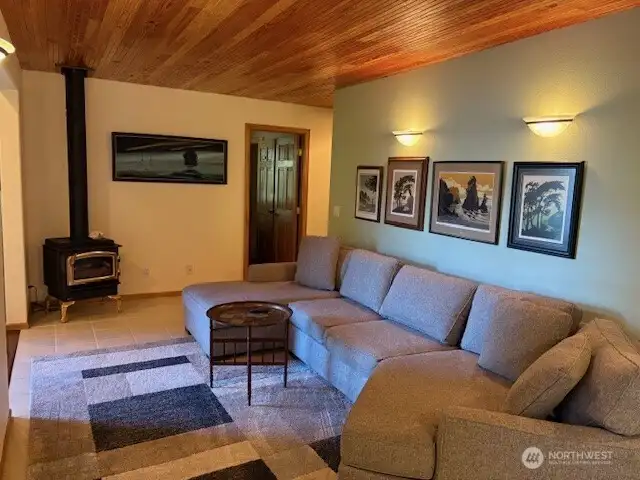 Living room area with tile flooring, beadboard wood ceiling, and freestanding propane stove.