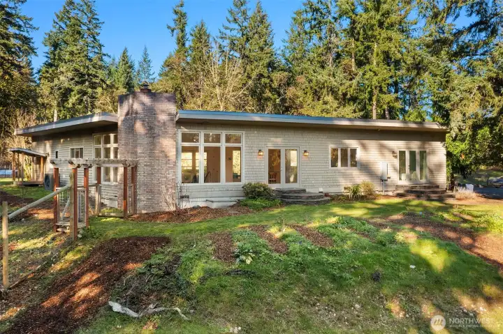 The soils in front of the home have been amended to support growing stellar veggies and fruits. Or, one could easily convert the terraces to a sloping lawn. Fenced area for pets can be seen to the left of the home.