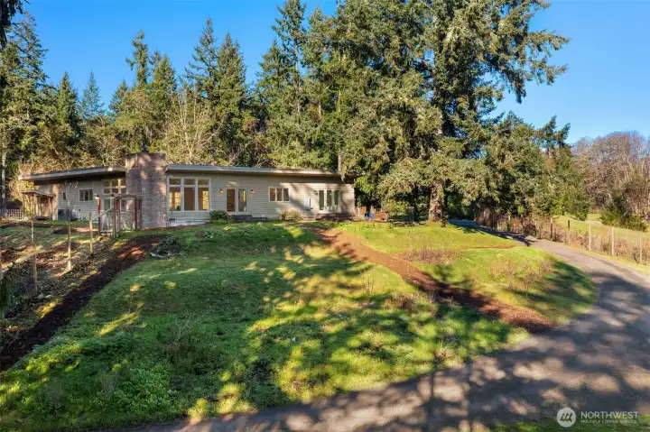 Drive curves around to the entrance to the fenced entry garden, garage and studio. This is the east-facing side of the home. Sun streams into the home in the mornings. Full southern sun almost every day of the year.