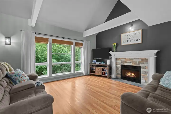 Spacious living room featuring vaulted ceilings, oversized windows, and greenbelt views
