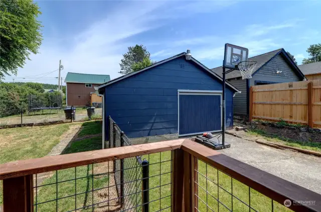 Corner peek at fenced back yard with alley behind. Garage with shop area.