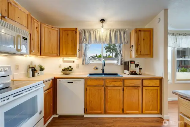 Light-filled kitchen features a large window over the sink, electric range, dishwasher and plenty of cabinet storage. (Virtually staged)