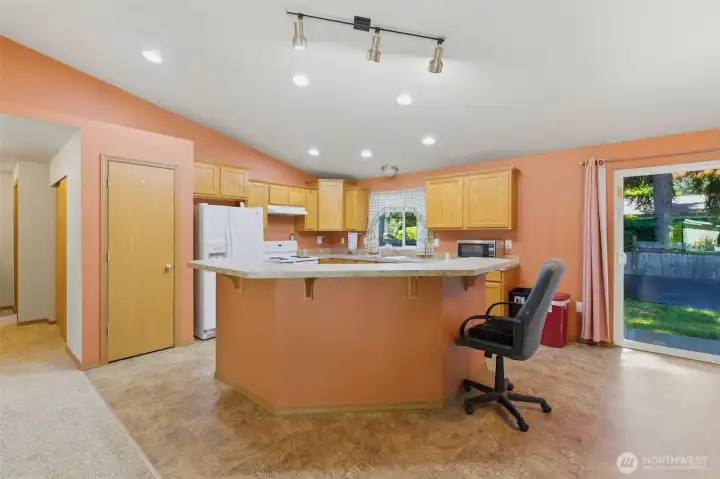 Bright open kitchen with peninsula breakfast bar, oak cabinetry, recessed and track lighting, and a slider to the backyard — great for entertaining