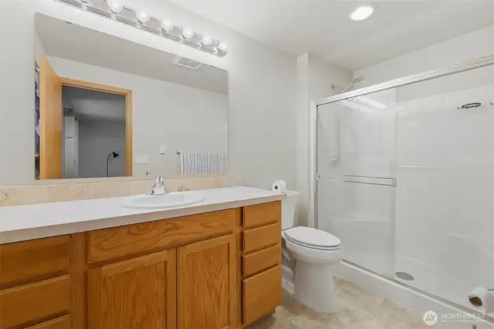 Primary en suite bath featuring an extended oak vanity, tile backsplash, walk-in glass shower, and warm recessed lighting