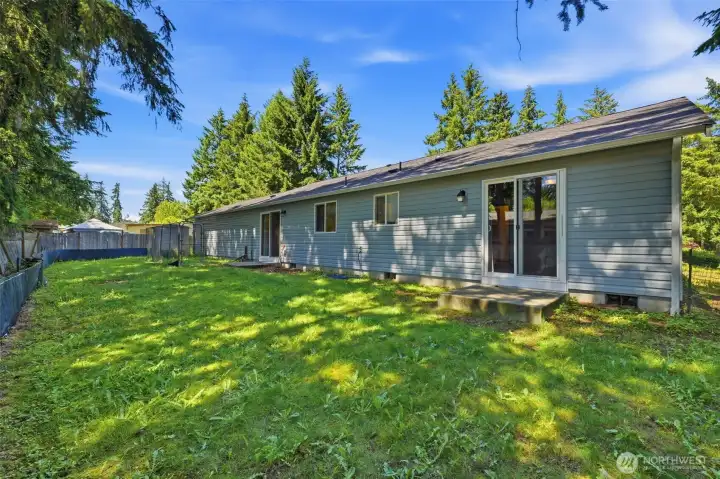 Generous fully fenced backyard with green lawn, mature tree canopy, and multiple access points — perfect for pets, play, and outdoor living.