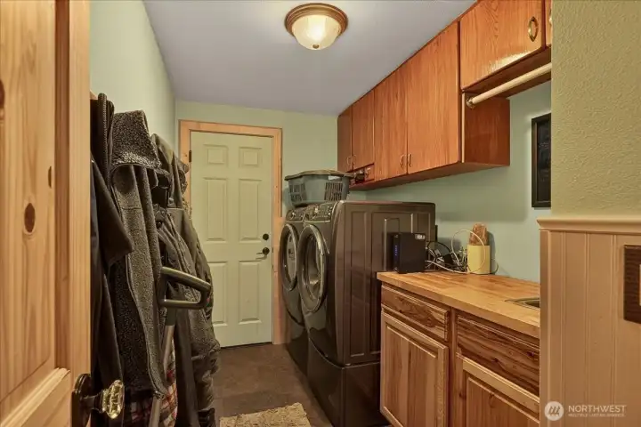 Mud room off garage with the washer dryer and sink with butcher block countertops and cupboards over washer dryer to keep supplies tucked away.