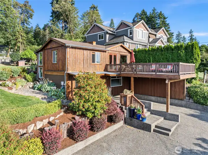 Side view of this charmer and view deck over the carport and paved parking area. A side walkway takes you up to the back entrance and upper level when separate entry is desired.