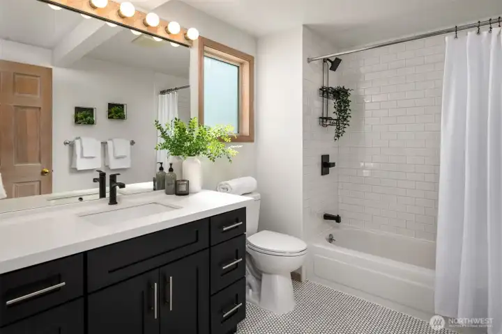 The main bathroom located upstairs is updated and bright with a large vanity, button tile floors and subway tile in the bath.