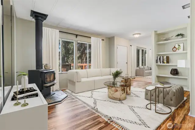 Family room with a woodstove and laminate flooring overlooks the community greenbelt.  Virtually staged photo.