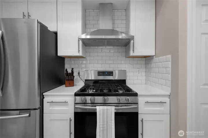 Gas range, stainless hood, and subway tile backsplash bring clean, modern style to the kitchen.