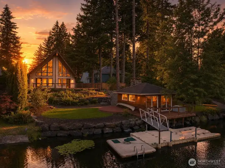 As the sun slips behind the evergreens, this enchanting waterfront retreat transforms into a scene worthy of a storybook—where the boathouse glows, the creek sparkles, and the day's final paddle home feels like pure magic.