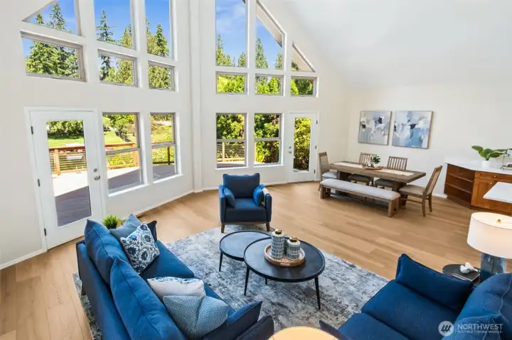Architectural drama abounds in the light-filled great room, where soaring ceilings, expansive windows, warm LVP-wood floors, and French doors to the deck create an inviting space that feels connected to nature and perfectly suited for waterfront living.