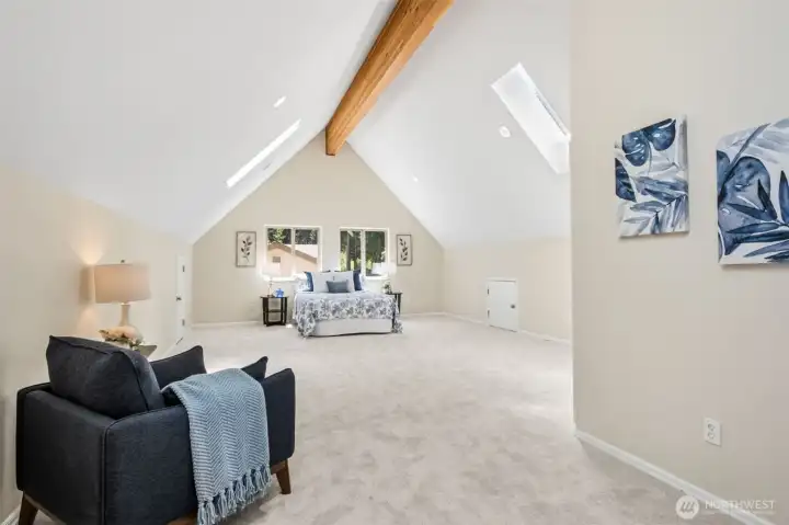 Occupying the entire upper level, the oversized bedroom suite offers a peaceful escape with soaring ceilings, architectural beam detail, plush newer carpeting, skylights, and generous flex space for reading, relaxing, or working from home.