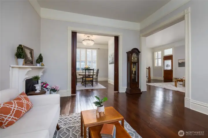 Elegant living space with rich wood floors, a classic fireplace, and wide openings leading to the dining room and entryway, showcasing the home’s timeless Victorian millwork.
