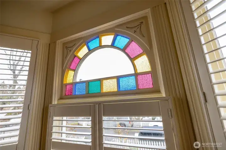 Colorful arched stained-glass transom window framed by detailed Victorian trim.