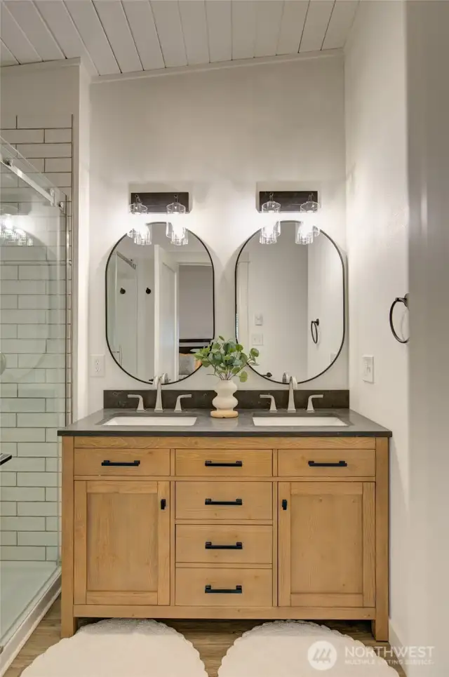The master bathroom boasts a double sink vanity, a tiled shower, and a sleek glass enclodure.