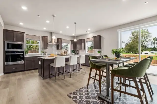Large open kitchen with quartz countertops, stainless steel appliances, gas cooktop, gourmet hood vent, and hardwood floors throughout. Photo is representational. Actual home is under construction and finishes will vary. See site agent for details.