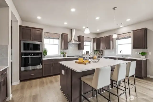 Large open kitchen with quartz countertops, stainless steel appliances, gas cooktop, gourmet hood vent, and hardwood floors throughout. Photo is representational. Actual home is under construction and finishes will vary. See site agent for details.