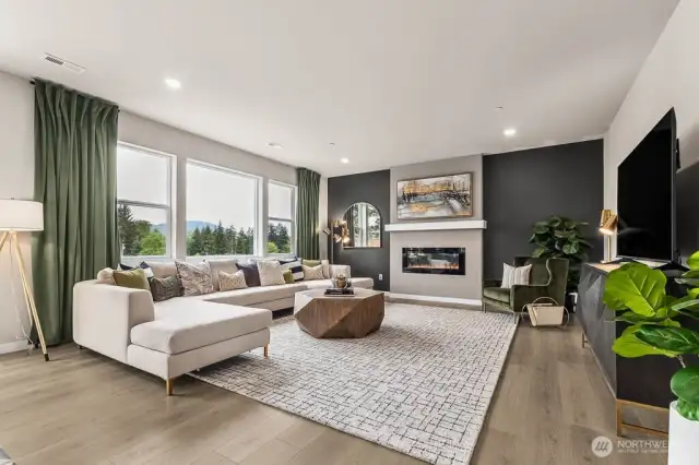 Great room with large windows allows natural light to fill the space. Fireplace with space for television above with hidden 110 outlet included. Photo is representational. Actual home is under construction and finishes will vary. See site agent for details.