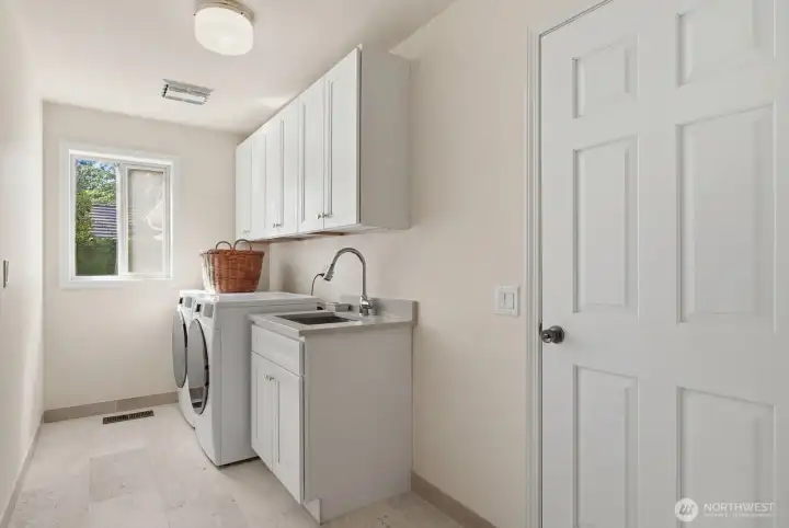 The spacious laundry room has been updated with limestone flooring, new cabinetry, deep stainless steel utility sink and quartz counter.