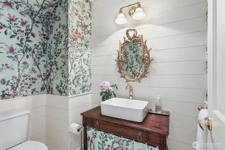 The ½ bath - powder room is adorned with Antoinette Poisson wallpaper, matching textile sink skirt, antique vanity, ship lap walls and marble floor.