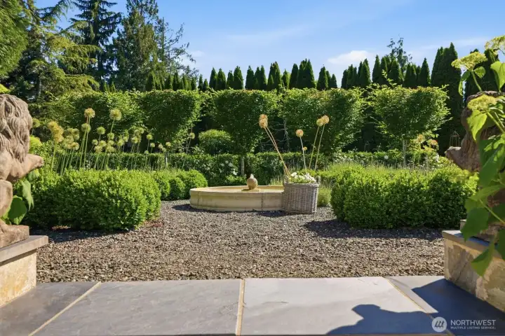 Gravel paths lead to a stunning 53-inch stone basin fountain, the centerpiece of a beautifully designed garden.