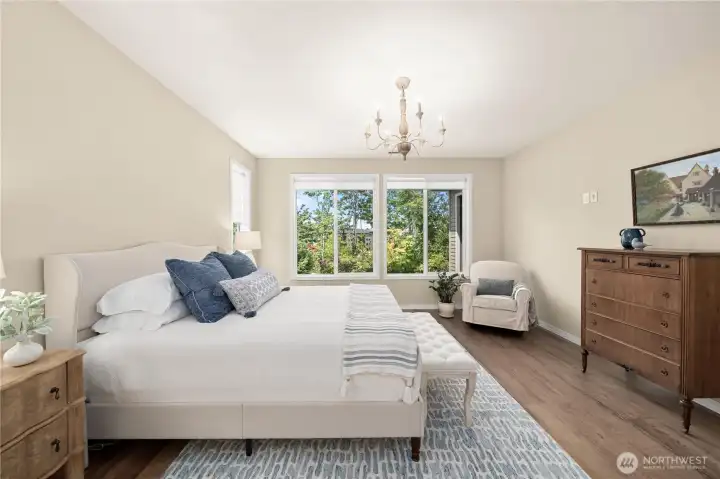 The generous primary suite enjoys scenic views, seamless wide plank flooring, a custom chandelier and roller shades (throughout the home). The generous primary suite enjoys scenic views, seamless wide plank flooring, a custom chandelier and roller shades (throughout the home).