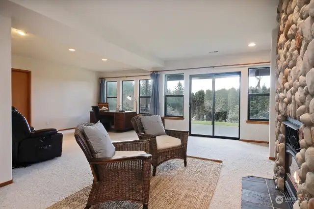 Veiw of the lower level Family Room with a wall of windows & glass door entry. One bedroom is to your back and the other is to your right, on the other side of the fireplace. There is a spacious storage closet, see door on the left edge of this photo.