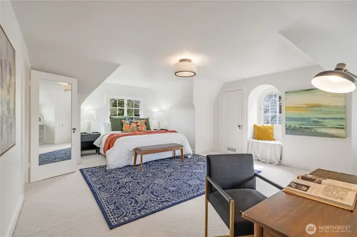 Huge upstairs primary suite with coved ceilings and windows, south and east facing light, pictured here with a king bed. Opens to an oversized walk-in closet with built-in desk, cabinets, and drawers.
