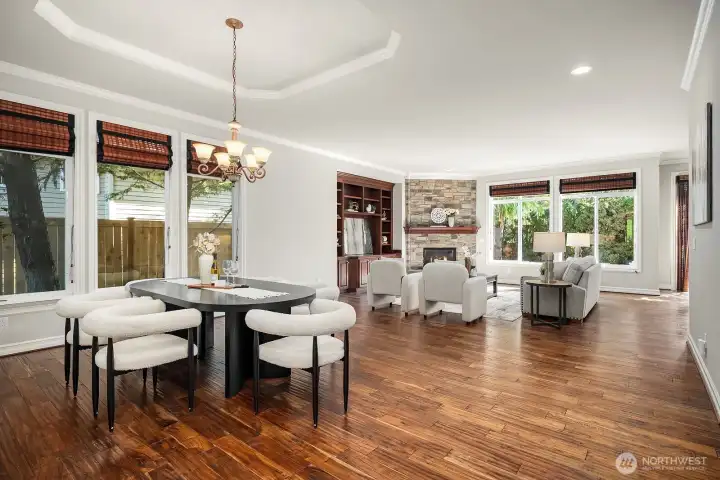 The elegant dining room is bathed in natural light from expansive windows, featuring a striking chandelier, rich acacia hardwood floors, and a coffered ceiling that adds architectural depth and refinement. This generously sized space flows effortlessly into the main living areas, making it perfect for both intimate dinners and large-scale entertaining.