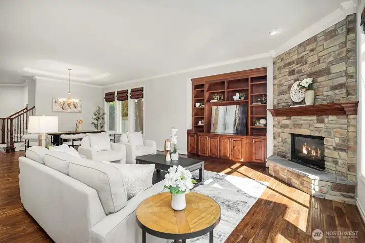 This inviting angle of the great room highlights the effortless flow between the living area and the gourmet kitchen beyond, creating an ideal open-concept layout for everyday living and entertaining. Rich built-ins, a stunning stone fireplace, and warm acacia hardwoods tie the spaces together with timeless, cohesive elegance.