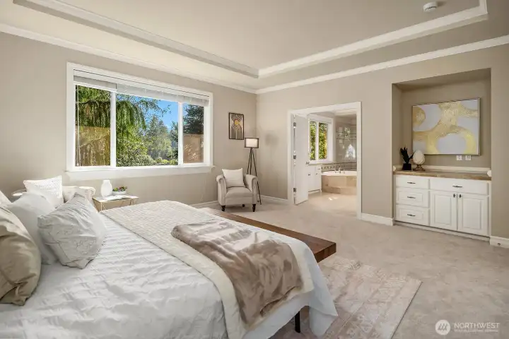 This angle of the expansive primary suite highlights the generous proportions of the space, with large windows flooding the room with natural light and offering tranquil views of the surrounding landscape. A glimpse of the dual walk-in closets beyond underscores the thoughtful functionality that makes this retreat as practical as it is luxurious.