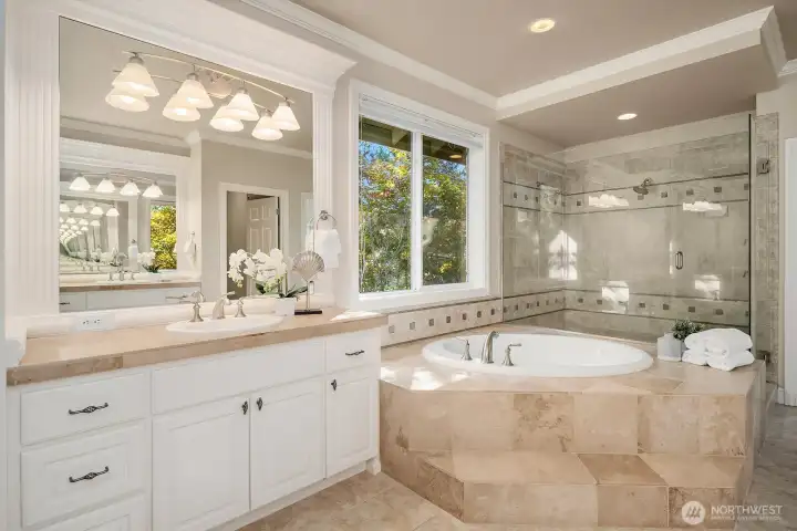 The spa-inspired five-piece primary bath is a showstopper, featuring dual vanities with abundant counter space, a luxurious soaking tub perfectly positioned beneath a sun-filled window, and a frameless glass steam shower. Elegant tile work, refined fixtures, and a soothing neutral palette come together to create a private retreat worthy of a five-star resort.