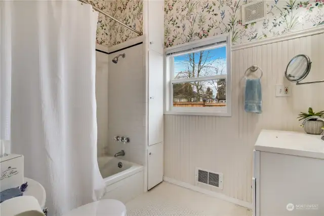 A new updated window lends a natural glow to the classic beadboard wainscotting, convenient built-in storage, and honeycomb tile work in this main floor bathroom.