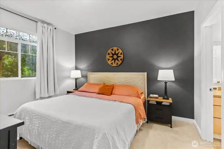 The spacious primary suite features soft neutral carpeting, a large window for natural light, and direct access to a private bathroom.