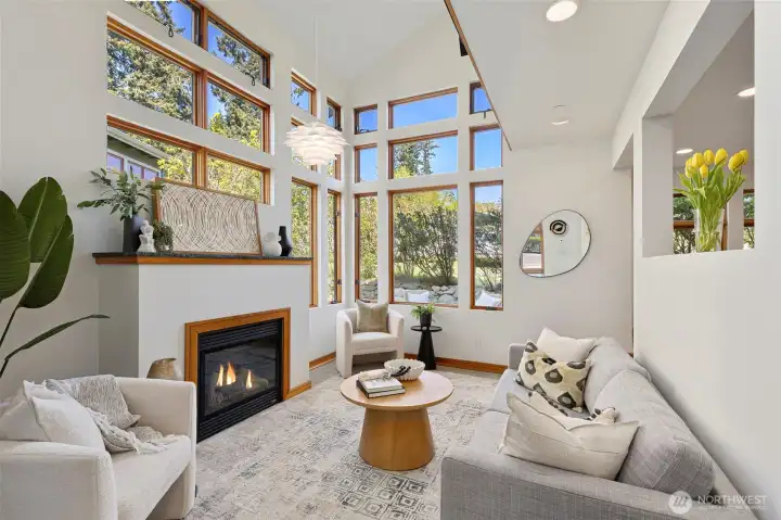 The propane fireplace anchors the living room beneath soaring ceilings and a grid of windows that flood the space with natural light.