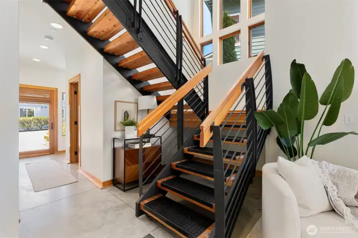 The open-tread staircase with steel frame and wood handrail is one of the home's standout architectural details, visible from both the entry and living area.