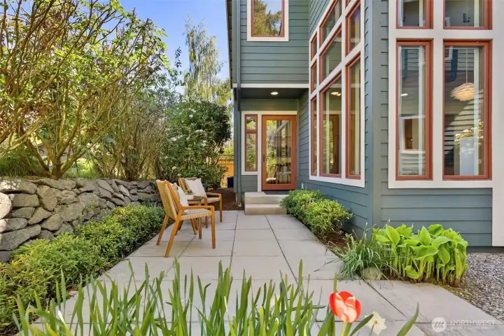 The private patio off the main level — concrete pavers, established plantings, a stone retaining wall, and a quiet sense of enclosure.