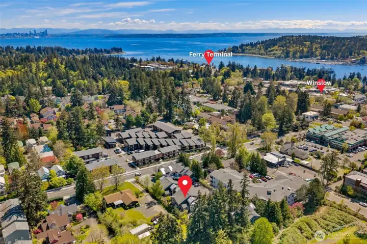 Winslow in the foreground, Eagle Harbor and the ferry terminal to the right, Seattle across the water, and Mount Rainier on the horizon. The commute context, in one frame.