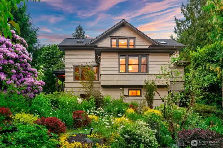 Step into your own private sanctuary — a breathtaking twilight garden alive with blooming rhododendrons, layered perennials, and lush mature plantings that wrap around this beloved 1922 Victorian-Craftsman.