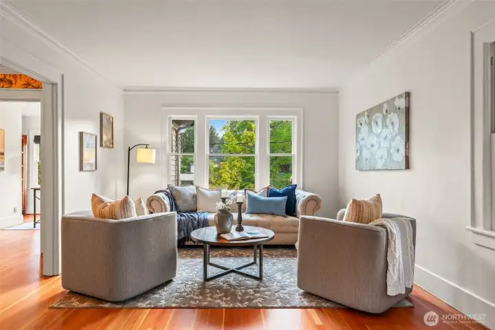 Curl up with a book or gather with friends in this sun-drenched living room, where gleaming original wood floors, elegant crown molding, and treetop views through a classic triple window set a warm, welcoming tone.