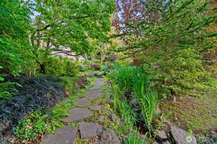 Wander through your own private woodland — a moss-edged stone path winds past ferns, ornamental grasses, irises, and a babbling creek, transporting you miles from the city without ever leaving home.